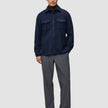 A man wears a Double Layer Wool Overshirt Regular Dark Navy over a brown turtleneck, paired with grey trousers and dark loafers.