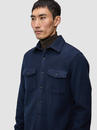 A man wearing a dark navy Double Layer Wool Overshirt Regular Dark Navy with two chest pockets over a dark brown turtleneck.
