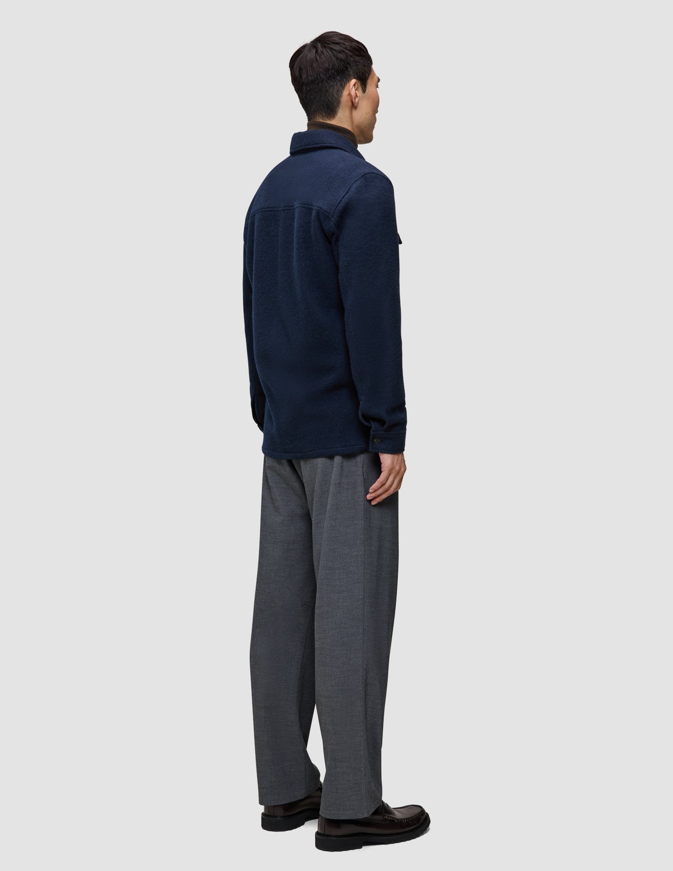 A person seen from behind wearing a Double Layer Wool Overshirt Regular Dark Navy, gray trousers, and dark shoes.