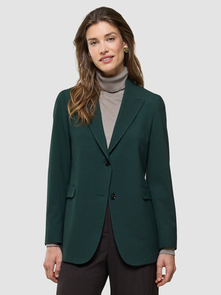 A woman wears a dark green Women Ease Blazer Evergreen over a beige turtleneck sweater.