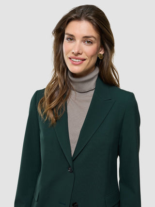A woman wearing a dark green Women Ease Blazer Evergreen over a beige turtleneck sweater, reflecting a minimalist Scandinavian design.