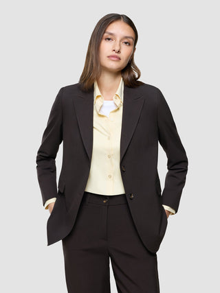 A woman wearing a Women Ease Blazer Mocha Melange over a light yellow button-up shirt and matching trousers with her hands in her pockets, reflecting a clean Scandinavian design.