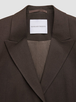 A brown Women Ease Blazer Mocha Melange with a label reading SHAPING NEW TOMORROW at the inner neckline, reflecting a minimalist Scandinavian design.