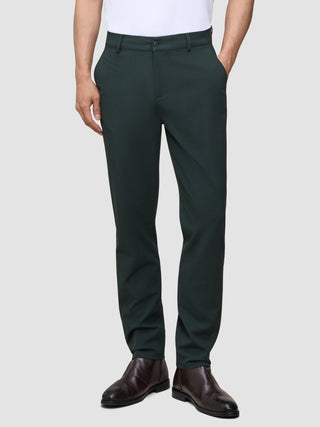 A person wears Ease Pants Regular Northern Pine dark green trousers and brown leather boots.