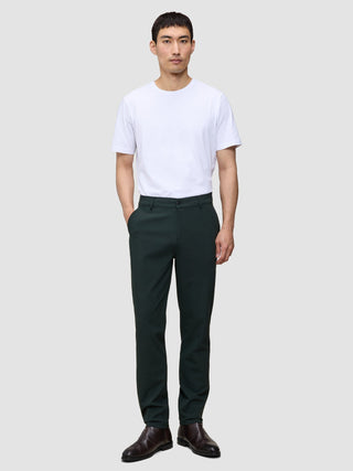 A person wearing a white t-shirt, Ease Pants Regular Northern Pine in dark green, and brown leather boots.