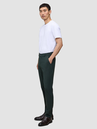 A person in a white t-shirt and dark green Ease Pants Regular Northern Pine stands in profile with one hand in their pocket.
