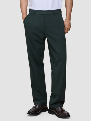 A person wearing exceptionally soft, dark green Ease Pants Relaxed Fit Northern Pine trousers and brown loafers.