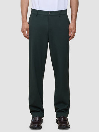 Person wearing exceptionally soft, dark green Ease Pants Relaxed Fit Northern Pine tailored trousers and dark loafers.