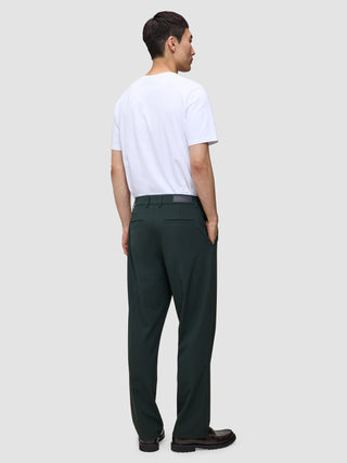 A man viewed from behind, wearing a white t-shirt and dark green Ease Pants Relaxed Fit Northern Pine with a tailored look, hands tucked into his pockets.
