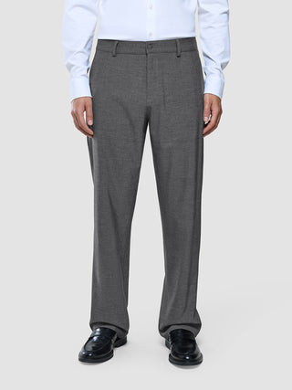 A man wearing a white dress shirt, Ease Pants Relaxed Fit Dark Grey, and black loafers.