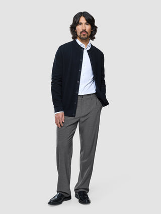 A man wearing a dark navy button-up cardigan over a white dress shirt and Ease Pants Relaxed Fit Dark Grey.