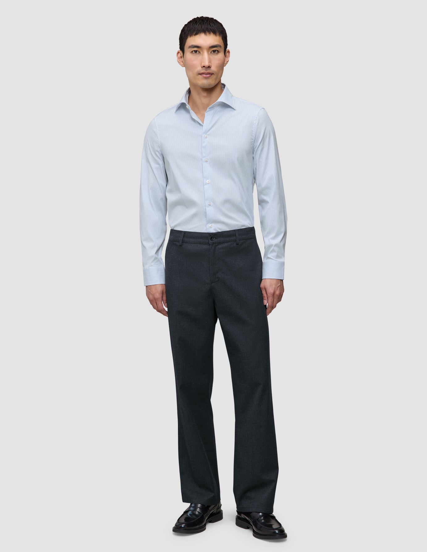 A man wearing an Elevated Shirt Slim Classic Blue Striped light blue button-up shirt with dark trousers and black loafers.
