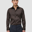 A man wearing a slim-fit dark brown Elevated Shirt Slim Dark Brown tucked into charcoal trousers.