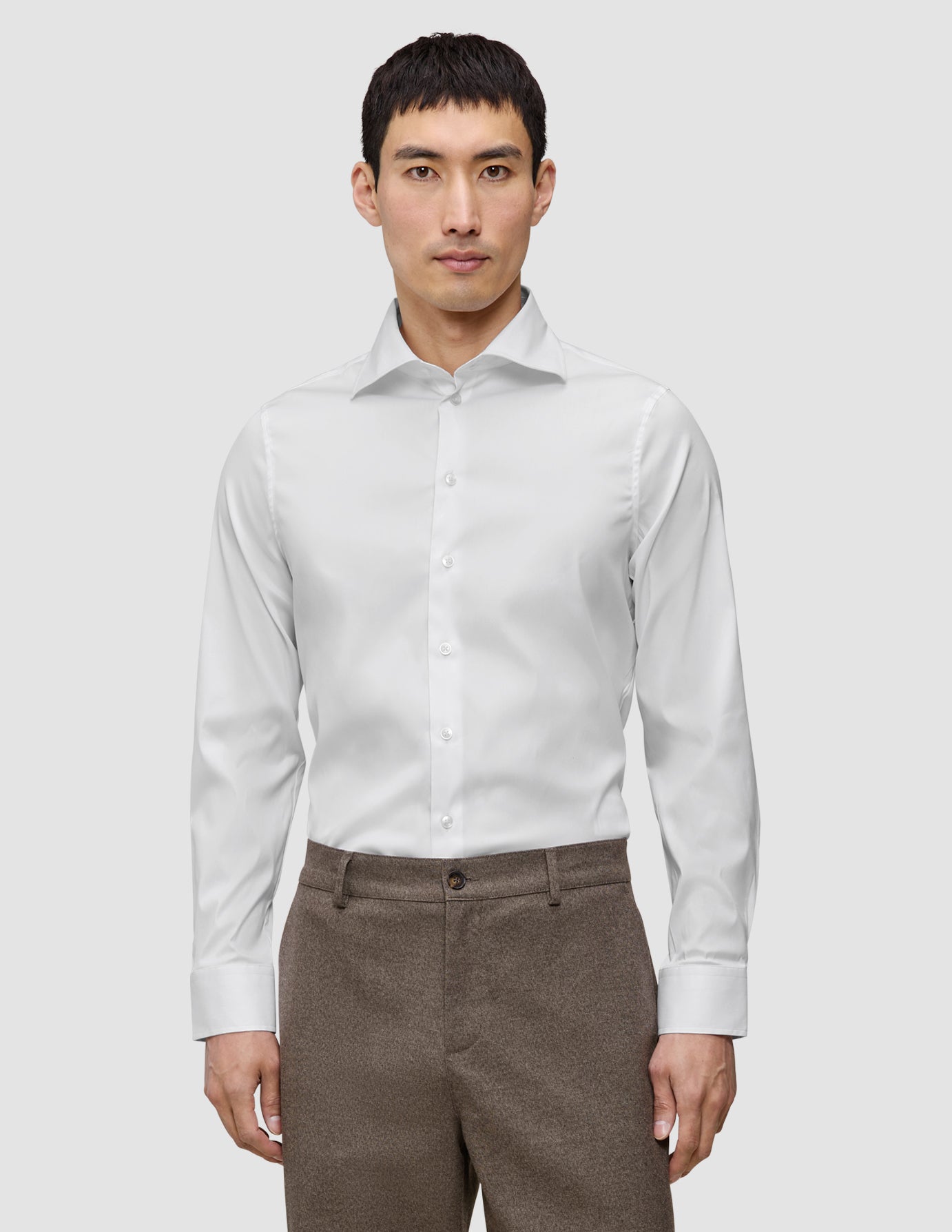A man wearing a slim fit, long-sleeved Elevated Shirt White Slim tucked into brown trousers.