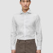A man wearing a slim fit, long-sleeved Elevated Shirt White Slim tucked into brown trousers.