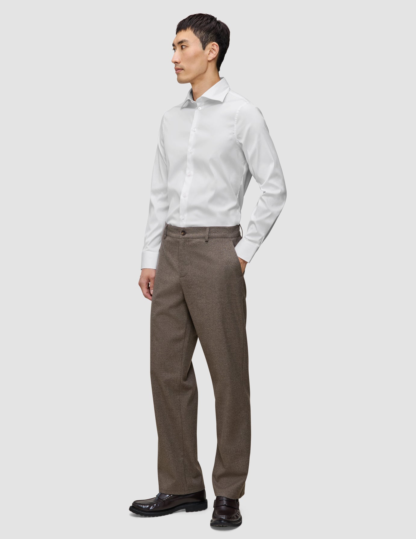A man wearing an Elevated Shirt White Slim tucked into brown trousers and dark loafers.