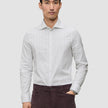 A man wearing an Elevated Shirt Slim Light Grey Striped, a light grey long-sleeved shirt with thin vertical stripes and dark trousers, reflecting a Scandinavian design aesthetic.