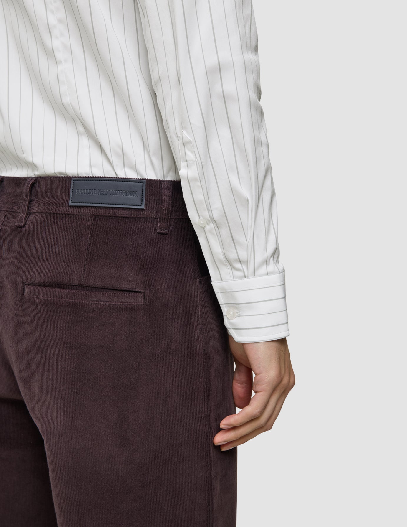 A person wearing an Elevated Shirt Slim Light Grey Striped, featuring a slim fit, white Pima cotton fabric with grey vertical stripes, tucked into dark brown corduroy trousers.