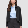 A woman wearing a black Essential Short Zip Jacket over a light blue button-down shirt.