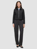 A woman wearing an Essential Short Zip Jacket Black over a light blue collared shirt, paired with charcoal grey trousers and black heels.