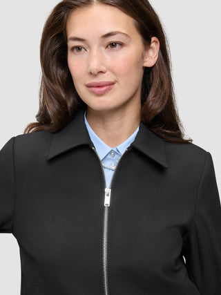 A minimalist black Essential Short Zip Jacket worn over a light blue button-down shirt.