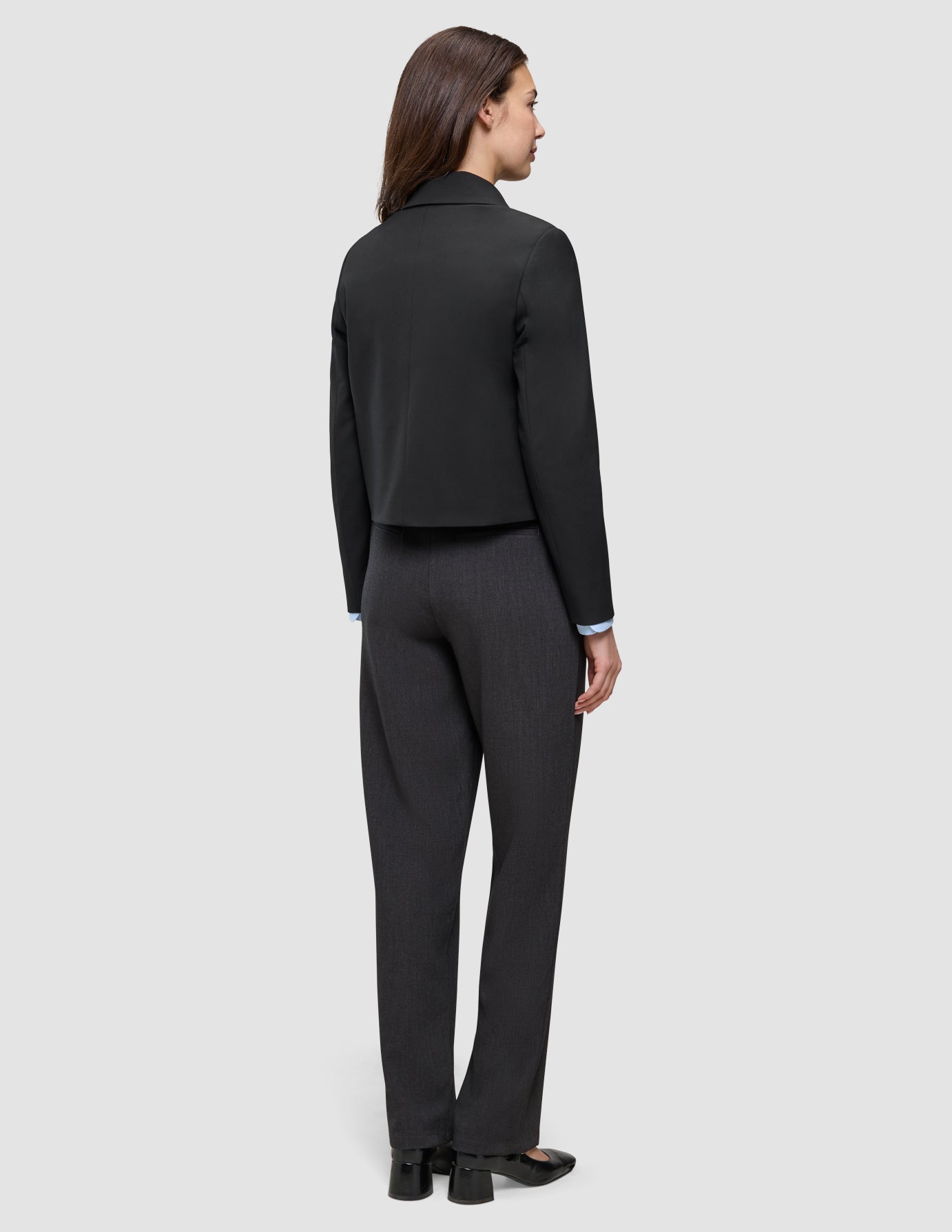 Back view of a person wearing an Essential Short Zip Jacket Black over a light blue button-down shirt and dark grey trousers.