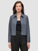 A person wears an Essential Short Zip Jacket Dark Grey Melange over a black top and trousers, showcasing a minimalist blazer aesthetic.