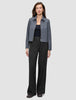 A woman wears a dark grey melange Essential Short Zip Jacket over a black top and wide-leg trousers.