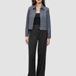 A woman wears a dark grey melange Essential Short Zip Jacket over a black top and wide-leg trousers.