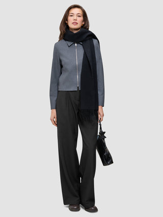 A person wearing an Essential Short Zip Jacket Dark Grey Melange, a black scarf, and black trousers, holding a black handbag.