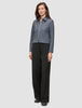 A woman wearing an Essential Short Zip Jacket Dark Grey Melange and loose black trousers.
