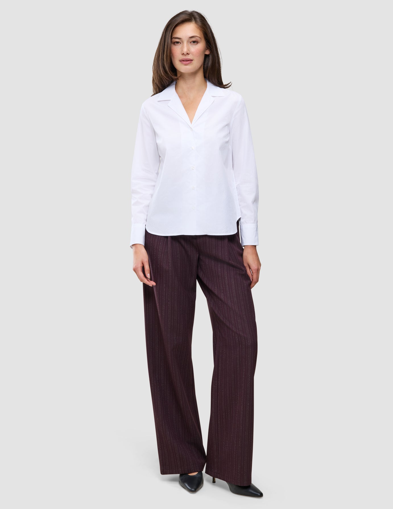 A woman wearing a white Madison Shirt with a notched collar and dark pinstriped wide-leg trousers.