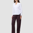 A woman wears the white Madison Shirt featuring a notched collar, paired with loose-fitting dark pinstriped trousers.