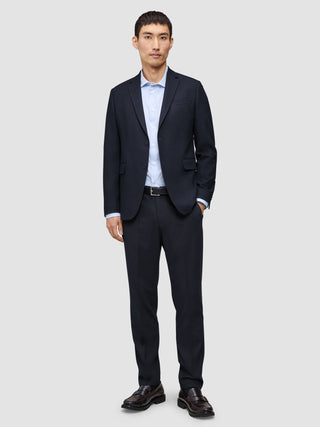 A man wearing a Motion Blazer Regular Midnight Blue and matching trousers over a light blue button-up shirt with dark leather loafers.