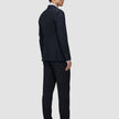 A person in profile wearing a Motion Blazer Regular Midnight Blue suit jacket and matching trousers over a light-colored dress shirt, paired with dark leather loafers.