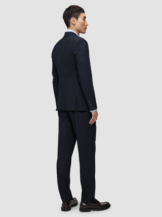 A person in profile wearing a Motion Blazer Regular Midnight Blue suit jacket and matching trousers over a light-colored dress shirt, paired with dark leather loafers.