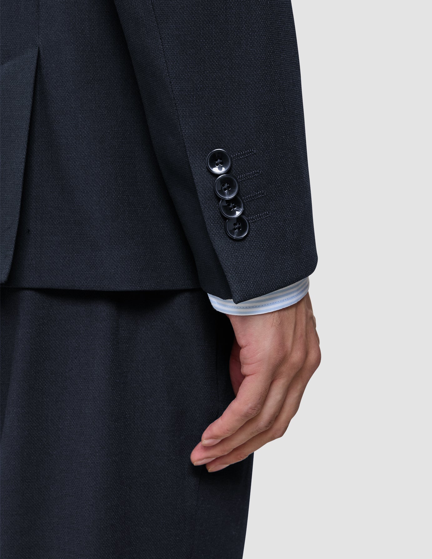 A dark blue sleeve of the Motion Blazer Regular Midnight Blue with four buttons at the cuff and a glimpse of a light-colored striped shirt sleeve underneath.