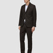 A man wearing a Motion Blazer Slim Cognac and matching trousers in lightweight breathable fabric, paired with a white button-down shirt and black dress shoes.