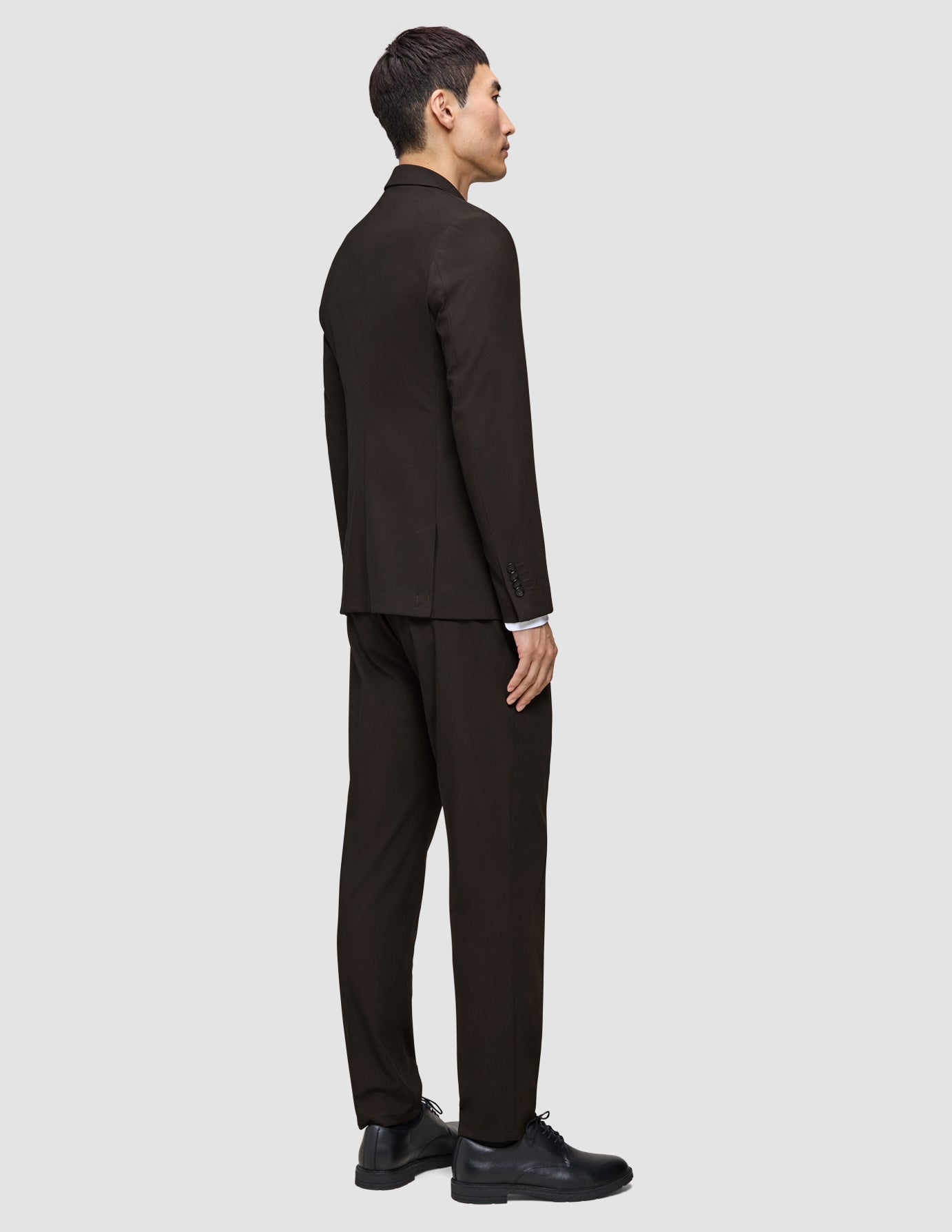 A person seen from the side wearing a Motion Blazer Slim Cognac in a lightweight, breathable brown fabric with a white shirt and black shoes.