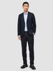 A man wearing a Motion Blazer Slim Midnight Blue with matching trousers, a light blue button-down shirt, a black belt, and brown loafers.