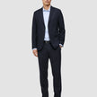 A man wearing a Motion Blazer Slim Midnight Blue with matching trousers, a light blue button-down shirt, a black belt, and brown loafers.