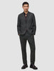 A man wears a Motion Blazer Slim Pepper Grey over a dark button-down shirt, with his hands in the pockets of the matching trousers.