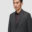 A man wears a Motion Blazer Slim Pepper Grey in a tailored, 360° stretch grey fabric over a dark brown button-up shirt.
