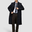 A man wearing a black overcoat, white dress shirt, dark tie, and Motion Suit Pants Regular Cognac.