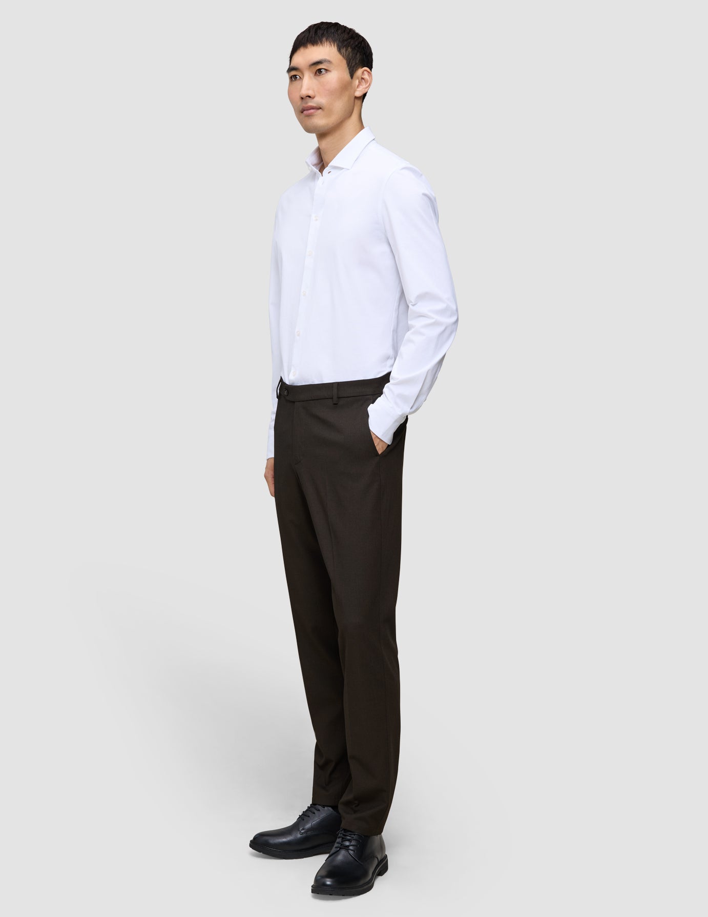 A man stands with his hand in his pocket wearing a white dress shirt and Motion Suit Pants Regular Cognac, which feature 360° stretch.