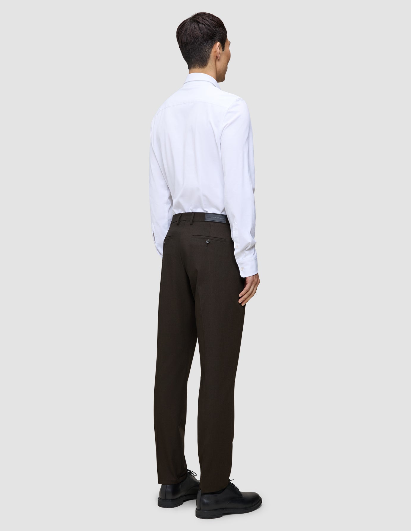 A person viewed from behind, wearing a white button-down shirt and Motion Suit Pants Regular Cognac with black dress shoes.