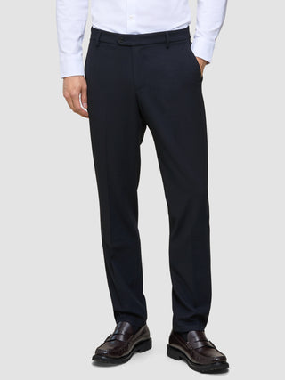 A man wearing a white dress shirt, Motion Suit Pants Regular Midnight Blue, and dark brown loafers.