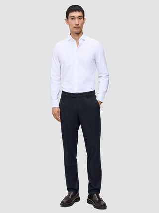 A man wearing a white button-down shirt, Motion Suit Pants Regular Midnight Blue, and dark leather loafers.