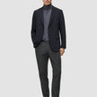 A man wears a black blazer, a grey turtleneck, and Motion Suit Pants Regular Pepper Grey, paired with a black leather belt and black loafers.