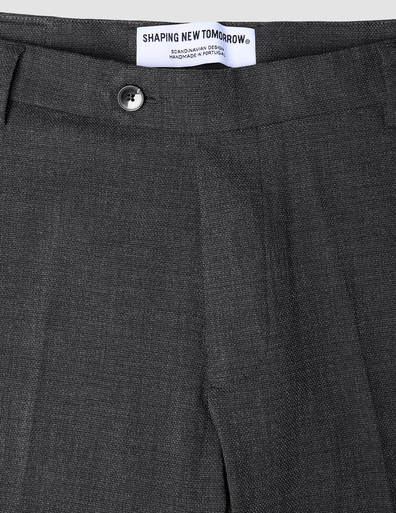 Close-up of Motion Suit Pants Regular Pepper Grey in charcoal grey 360° stretch fabric, featuring a button closure and a brand label at the waistband.